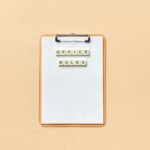 A clipboard with the phrase 'Office Rules' spelled out using Scrabble tiles on a beige background.