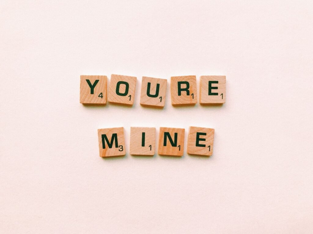 Romantic message You're Mine created with wooden Scrabble tiles on a pink background.