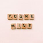 Romantic message You're Mine created with wooden Scrabble tiles on a pink background.