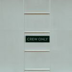 A minimalistic image featuring a 'Crew Only' sign on a ladder against a white wall.