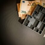 A top view of euro banknotes, a miniature architectural model, and a key symbolizing property investment.