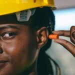 Close-up of a woman wearing a hard hat and fitting earplugs for safety on site.