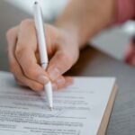 Detailed view of a hand writing a signature on an official document with a ballpoint pen.