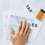 Close-up of a hand on tax form 1040 with a calculator on a desk.