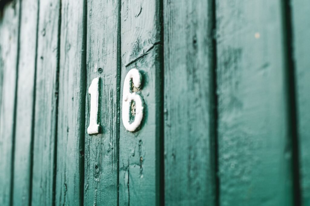 Close-up of a rustic green wooden wall with the white number 16 painted on it.