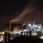 Illuminated refinery emitting smoke at night in Normandie, highlighting industrial impact.