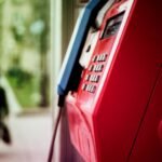 Vibrant red public telephone booth in urban setting with blurred background.