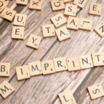 Wooden Scrabble tiles arranged on a wooden surface, spelling 'Imprint'.
