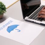 Close-up of hands typing on laptop with an insurance document visible on the desk.
