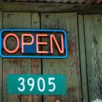 Close-up of a red neon open sign and address on rustic wooden wall.
