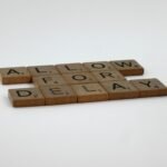 Wooden Scrabble tiles arranged on a white surface spelling 'Allow for Delay'.