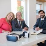 Elderly couple smiling with real estate agent during home meeting, showcasing modern technology.
