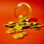 A collection of golden coins spilling from a glass jar on a vibrant red background symbolizes wealth.
