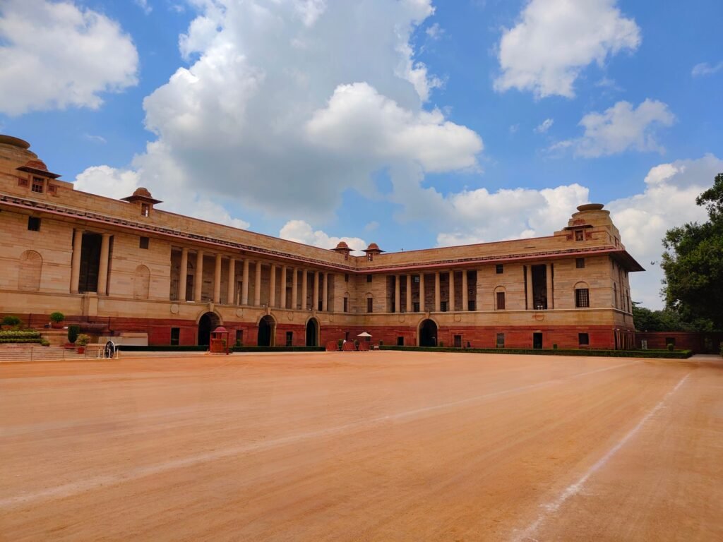 Wide view of Rashtrapati Bhavan in Delhi, India on a sunny day with blue skies and white clouds.