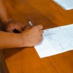 Close-up of hands signing a legal document on a wooden table indoors.