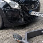 A damaged car and scooter after a collision in an urban setting.