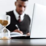Businessman at desk with hourglass indicating time management and daily work routine.