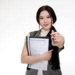 Asian woman smiling while holding a home insurance policy and a key, symbolizing new home ownership.