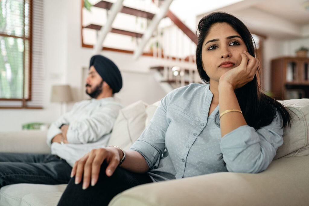 Young Indian couple sitting on different sides of couch and ignoring each other after arguing at home