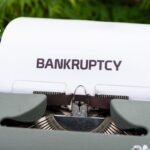 Close-up of a typewriter with the word 'BANKRUPTCY' on paper, surrounded by greenery.