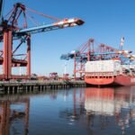 Container ship at Hamburg port with cranes on a clear day, showcasing industrial operations.