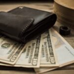 Close-up view of a leather wallet with US dollar bills on a wooden table.