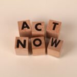 Wooden blocks with letters spelling 'ACT NOW', promoting urgency and motivation.