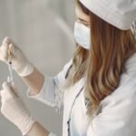 A female scientist in protective gear prepares a vaccine injection in a laboratory setting.