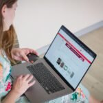 Woman in floral dress shopping online with a laptop and credit card indoors.