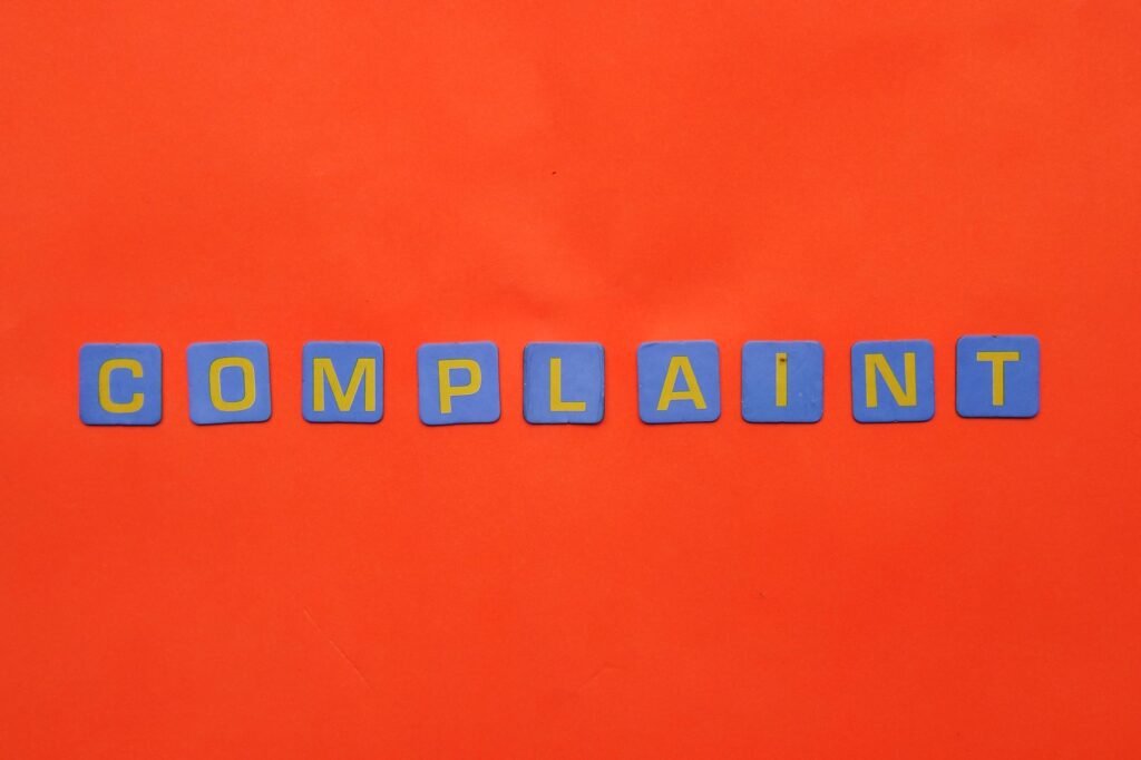 Blue letter tiles spelling 'COMPLAINT' on a vibrant red surface.