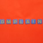 Blue letter tiles spelling 'COMPLAINT' on a vibrant red surface.