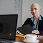 Serious young woman in formal clothes sitting at table and working with documents in office