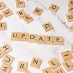 Wooden Scrabble tiles arranged to spell 'Update' among scattered letters on a marble background.