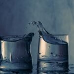 Close-up of splashing water between two glasses on a blue background.