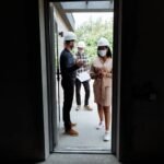 Real estate agents discussing a property at a construction site with safety measures in place.
