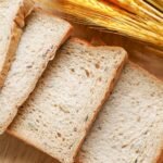 Close-up of sliced whole grain bread on a wooden surface with wheat ears.