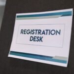 A close-up of a registration desk sign on a dark background.