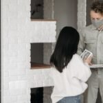 A man in a mask delivers a package to a woman at home, reflecting pandemic safety measures.