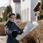 Woman examining a blueprint in a sunny residential area, considering properties.