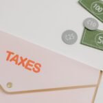 Pink envelope labeled 'TAXES' with play money and card on white background.