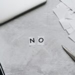 Top view of scattered paper squares, laptop, and scissors forming the word 'NO', implying rejection or denial.