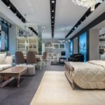 Interior of spacious furniture store with classic styled bed with coverlet and cushions placed in front of soft couch and dining table