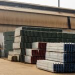 Outdoor view of an industrial warehouse with multiple stacks of metal beams and pallets.