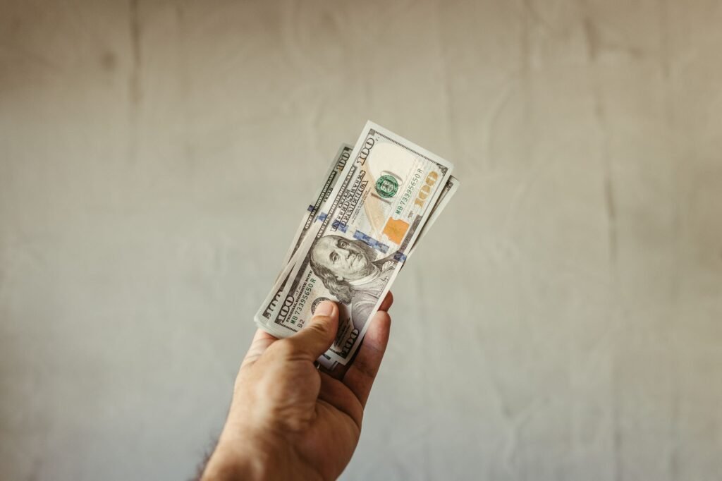 A hand holding a stack of US dollar banknotes against a neutral backdrop, symbolizing wealth.