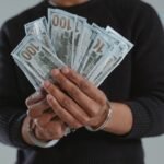 Close-up of hands holding 100-dollar bills while handcuffed, symbolizing crime and punishment.