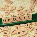 Wooden Scrabble tiles spelling 'UPDATE' with scattered tiles on a textured surface.