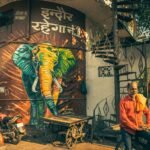 Vibrant street art featuring an elephant mural in Indore, India, with local men and a spiral staircase.