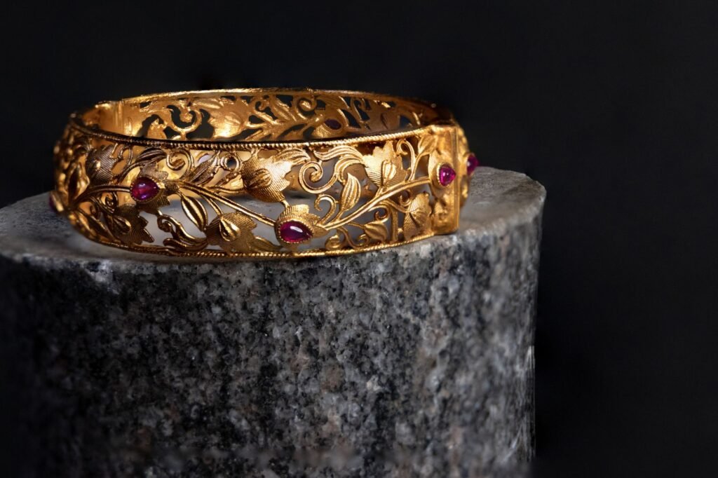 Intricate gold bracelet with ruby accents on a dark background. Luxurious and elegant design.