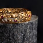 Intricate gold bracelet with ruby accents on a dark background. Luxurious and elegant design.