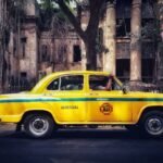 A classic yellow taxi parked in front of a dilapidated building, evoking nostalgia and urban charm.